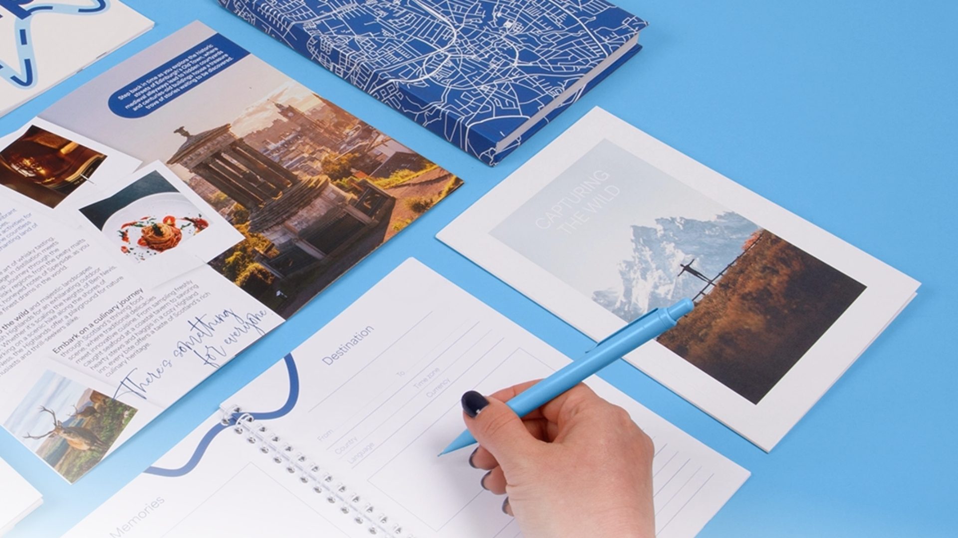 Hand writing in a custom printed travel planner surrounded by high-quality brochures and a map-patterned notebook.