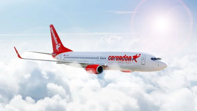 Corendon Airlines passenger aircraft flying against a clear blue sky, representing affordable holiday travel options.
