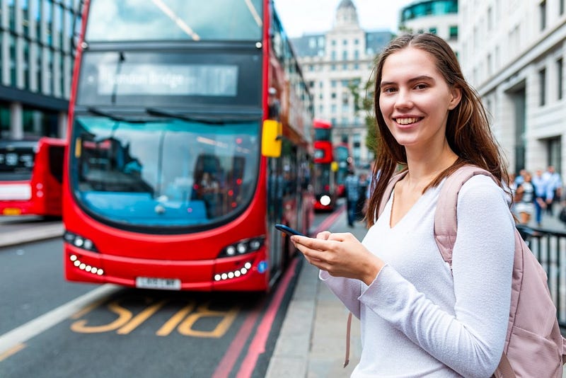 Passenger holding smartphone in front of an arriving red London double-decker bus