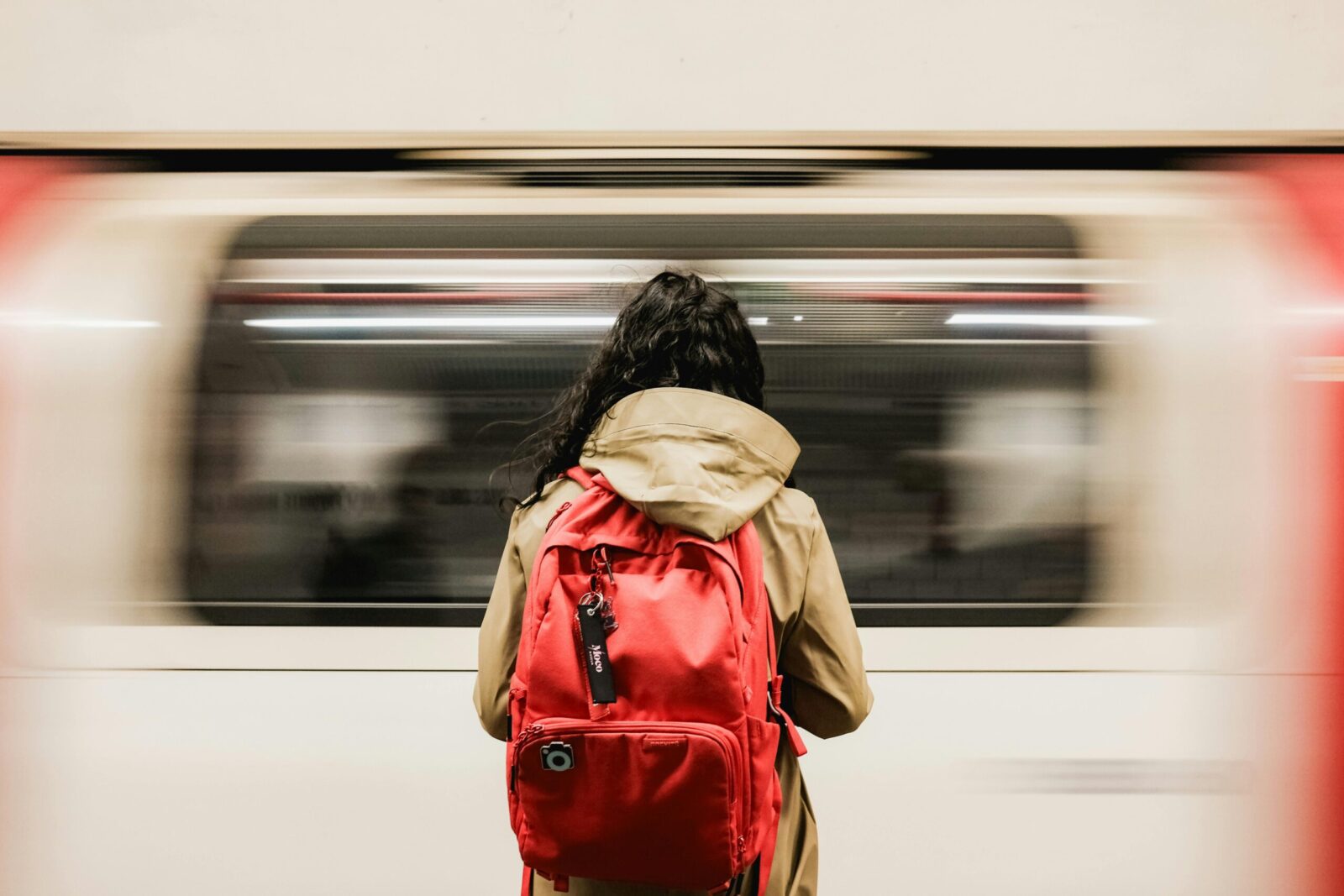 Commuter with red backpack on London Underground platform as tube train speeds past