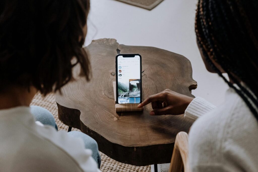 Adults explore social media on a smartphone resting on a unique wooden table.