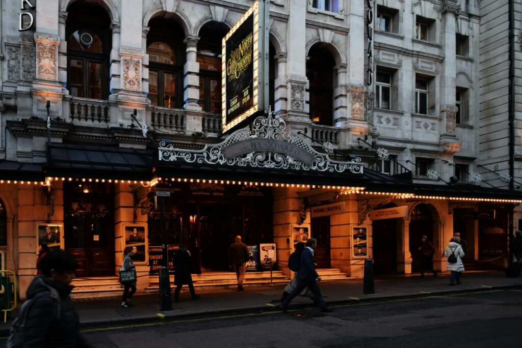 People walking past an illuminated West End theatre in Central London at night, ideal for theatre ticket deals.