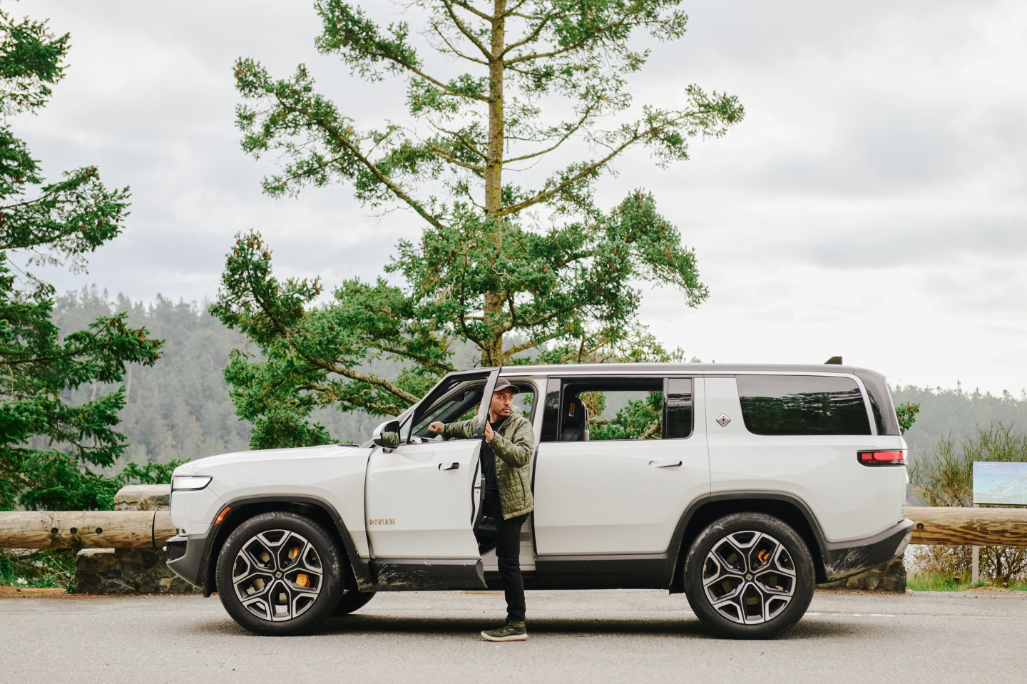 Driver stepping out of an electric Rivian SUV on a scenic road trip via Turo
