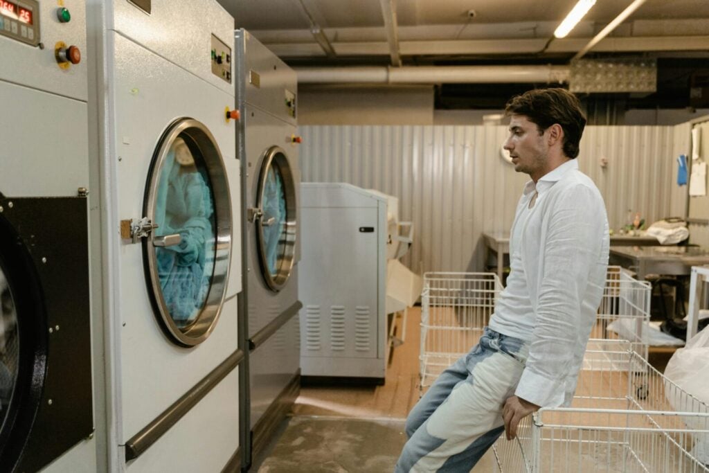A man sits patiently in a modern self-service laundrette, surrounded by large industrial washing machines, waiting for his laundry.