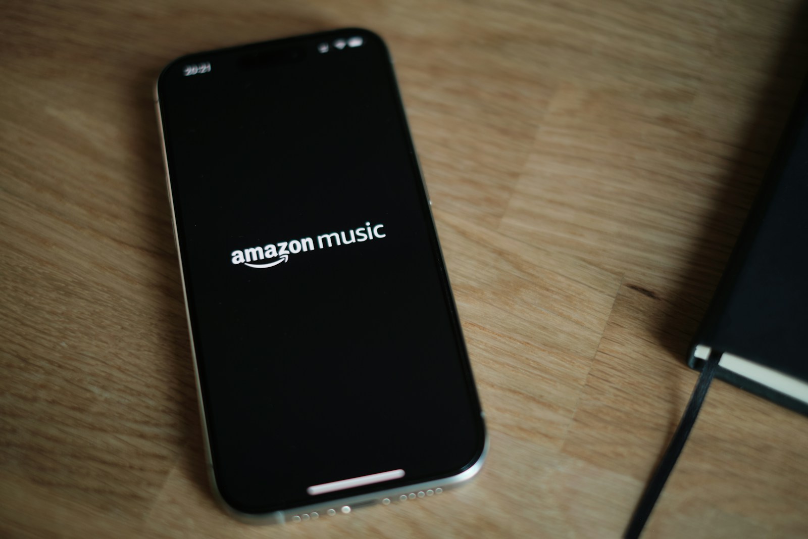 iPhone resting on a wooden desk displaying the Amazon Music streaming service app interface