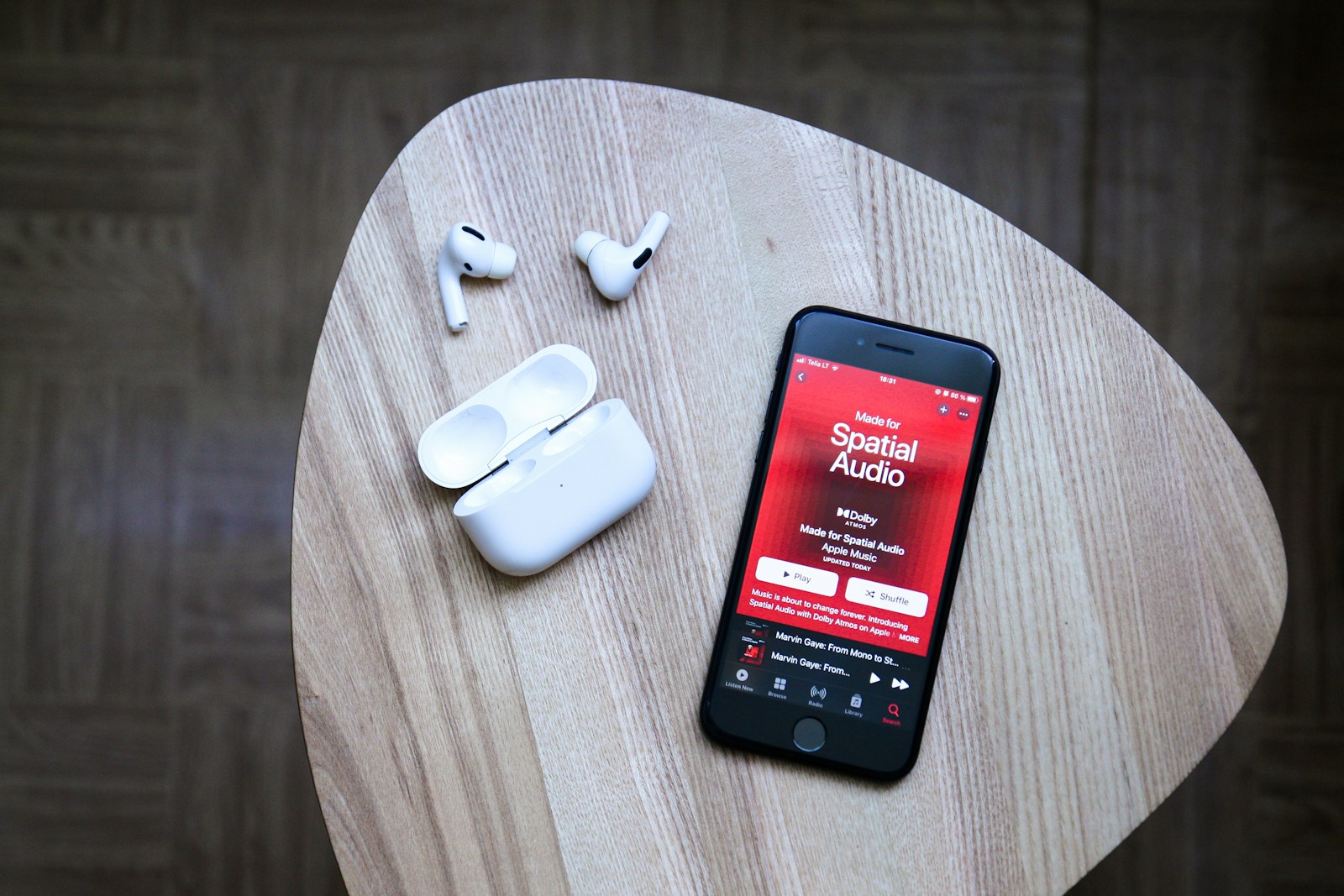 Apple iPhone displaying Apple Music Spatial Audio next to Apple AirPods Pro earphones
