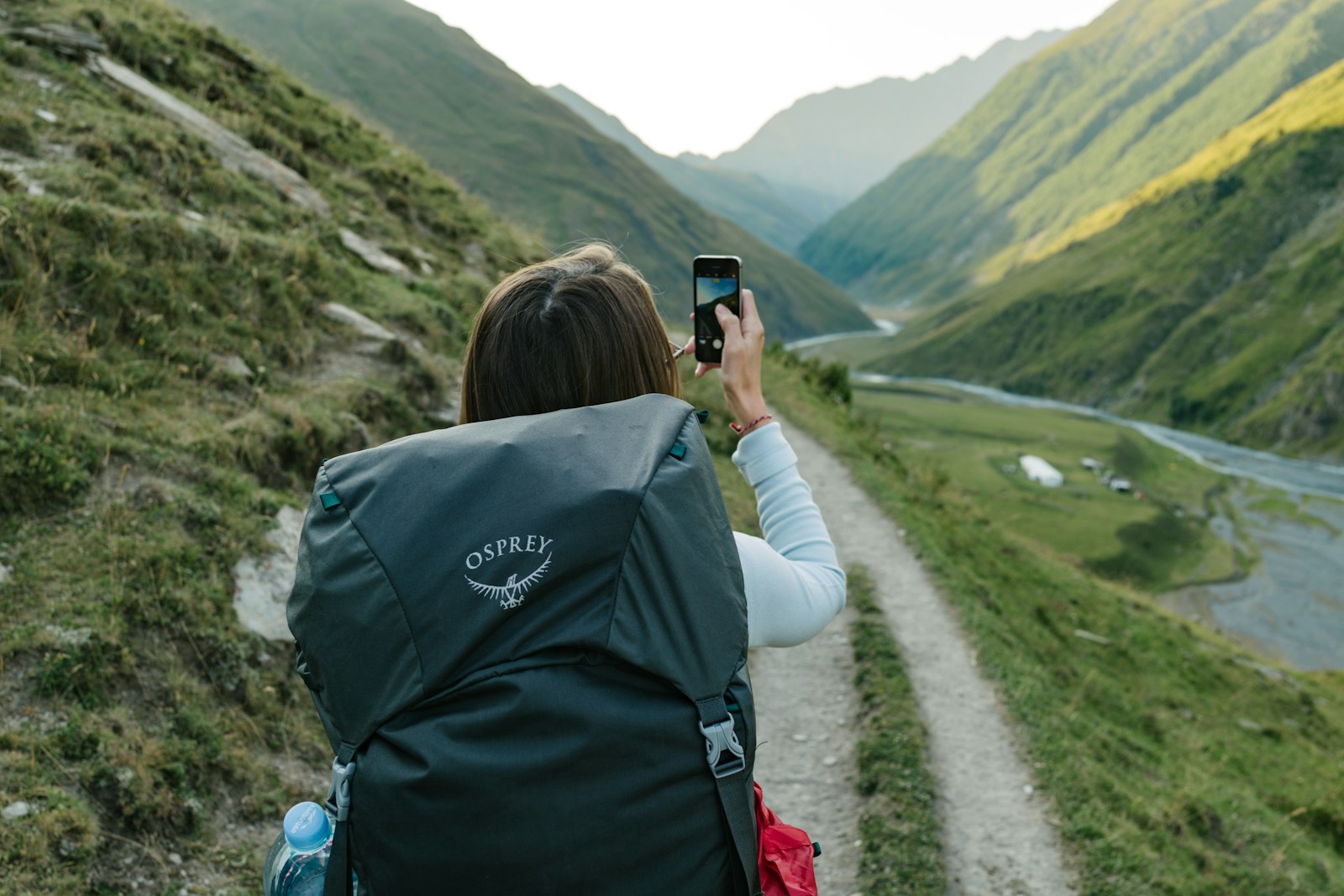 Woman backpacker taking photo with iPhone on a scenic mountain hike. Adventure travel photography in stunning natural landscape.