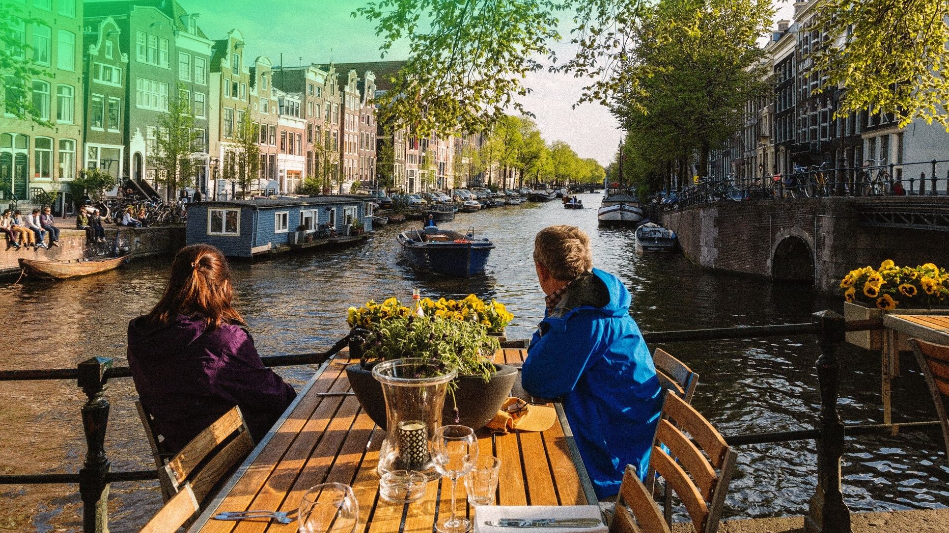 Couple sitting at a canal-side restaurant table overlooking the historic Prinsengracht canal in Amsterdam.