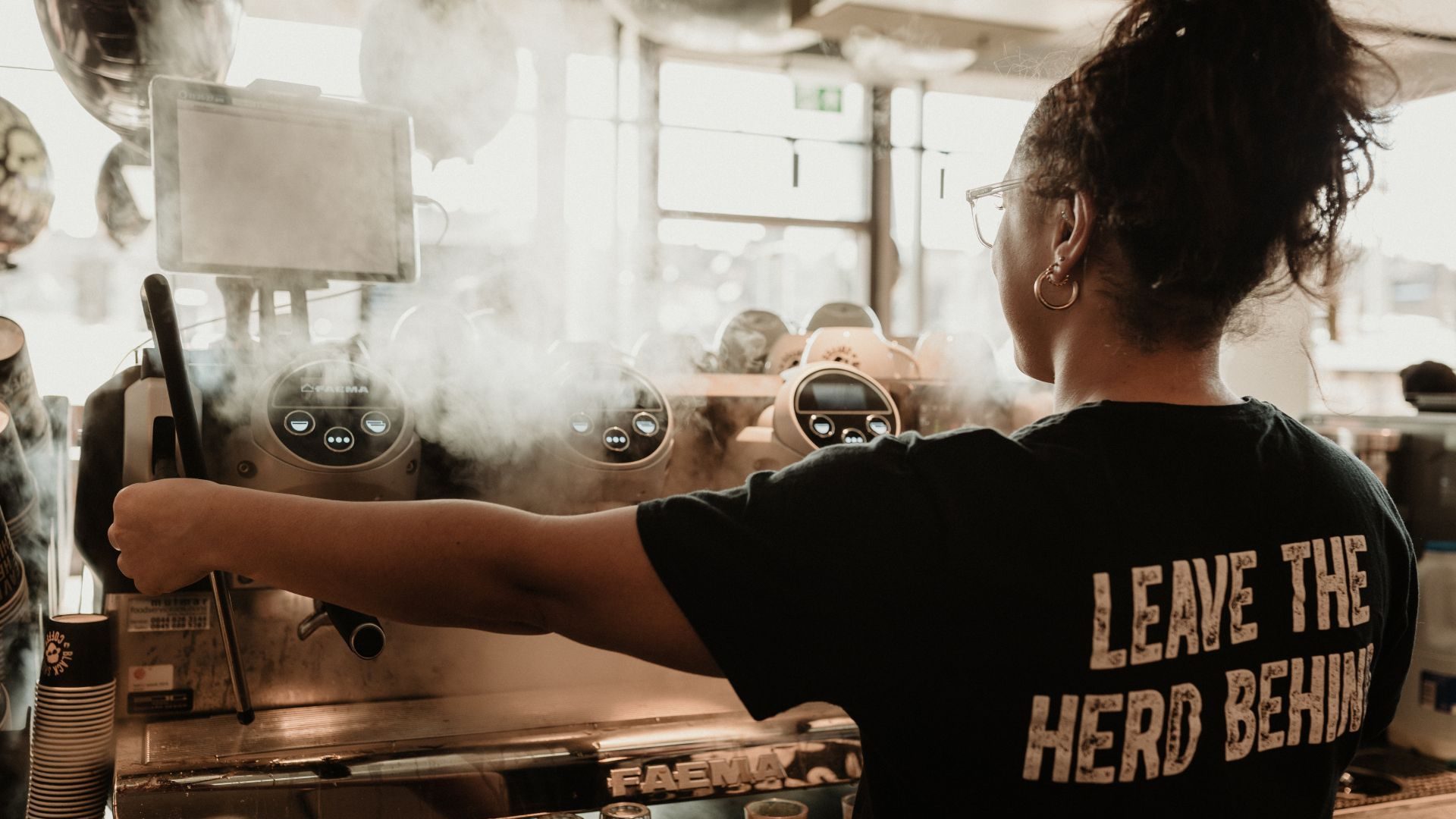 Barista wearing a Black Sheep Coffee uniform steaming milk on a professional Faema espresso machine in a UK cafe.