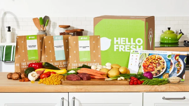 HelloFresh UK meal kit box with fresh ingredients and recipe cards on a kitchen counter for home cooking.