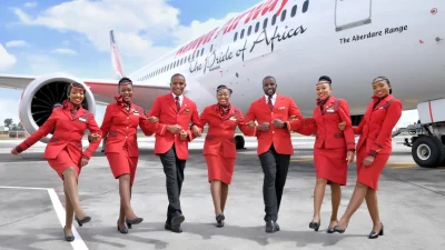 Kenya Airways aircraft parked at an international airport terminal, showcasing the airline's signature livery and branding.