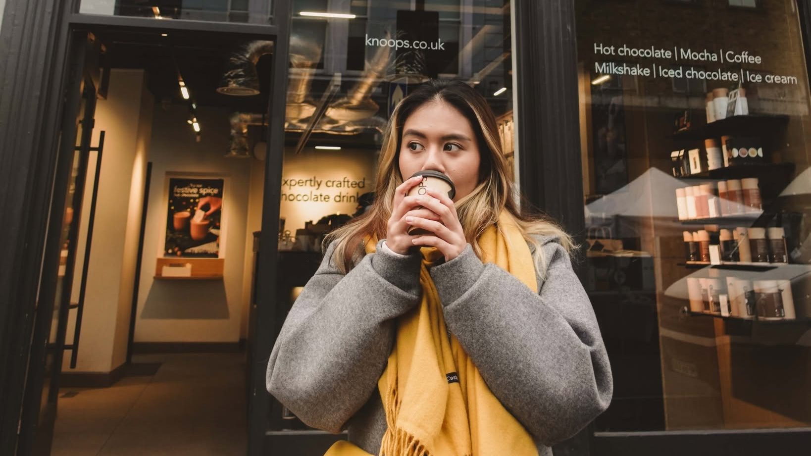 A woman drinking a Knoops artisan hot chocolate outside a London shopfront.