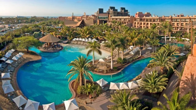 Lopesan Hotels luxury resort exterior featuring a swimming pool and tropical gardens under a bright blue sky.