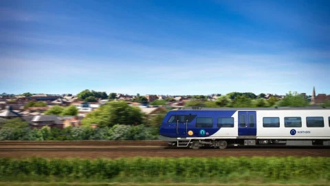 A modern Northern Railway train travelling through the scenic British countryside on a bright, sunny day.