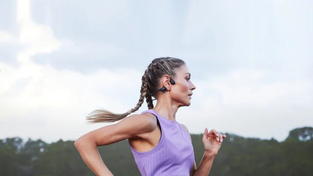 Person wearing Shokz bone conduction headphones while running outdoors, showcasing premium wireless audio technology.