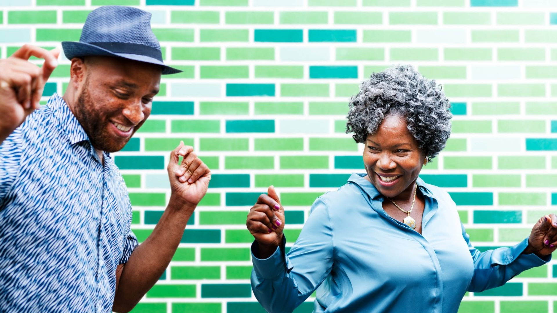 A smiling man and woman dancing joyfully in front of a vibrant green brick wall, representing mobile connectivity.