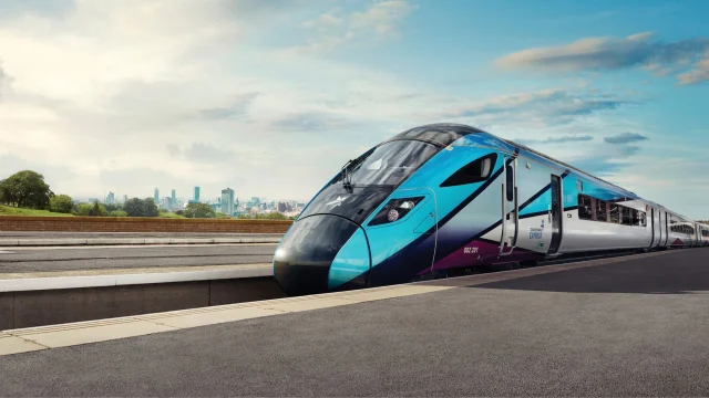 A modern TransPennine Express train travelling through the scenic British countryside on a bright day.