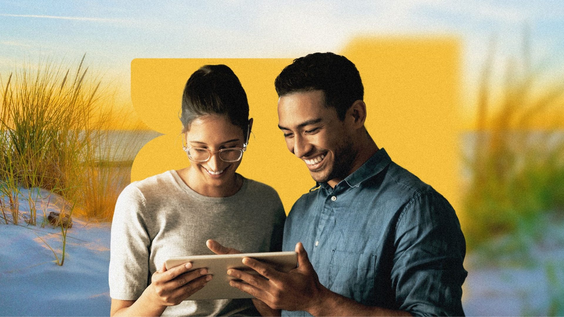 A smiling man and woman collaborating on a tablet device against a coastal background.