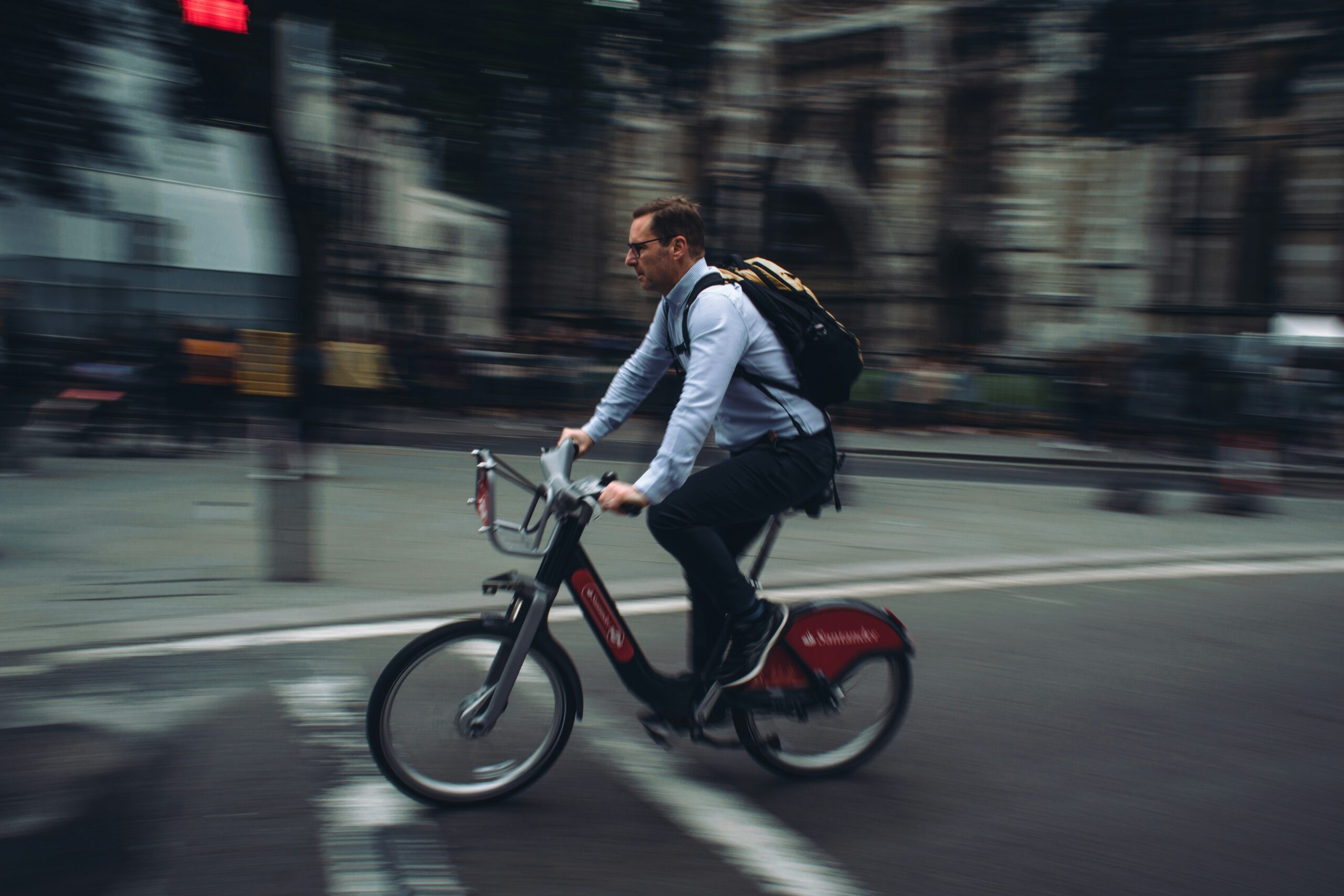 City commuter cycling on a red Santander hire bike past historic buildings in London