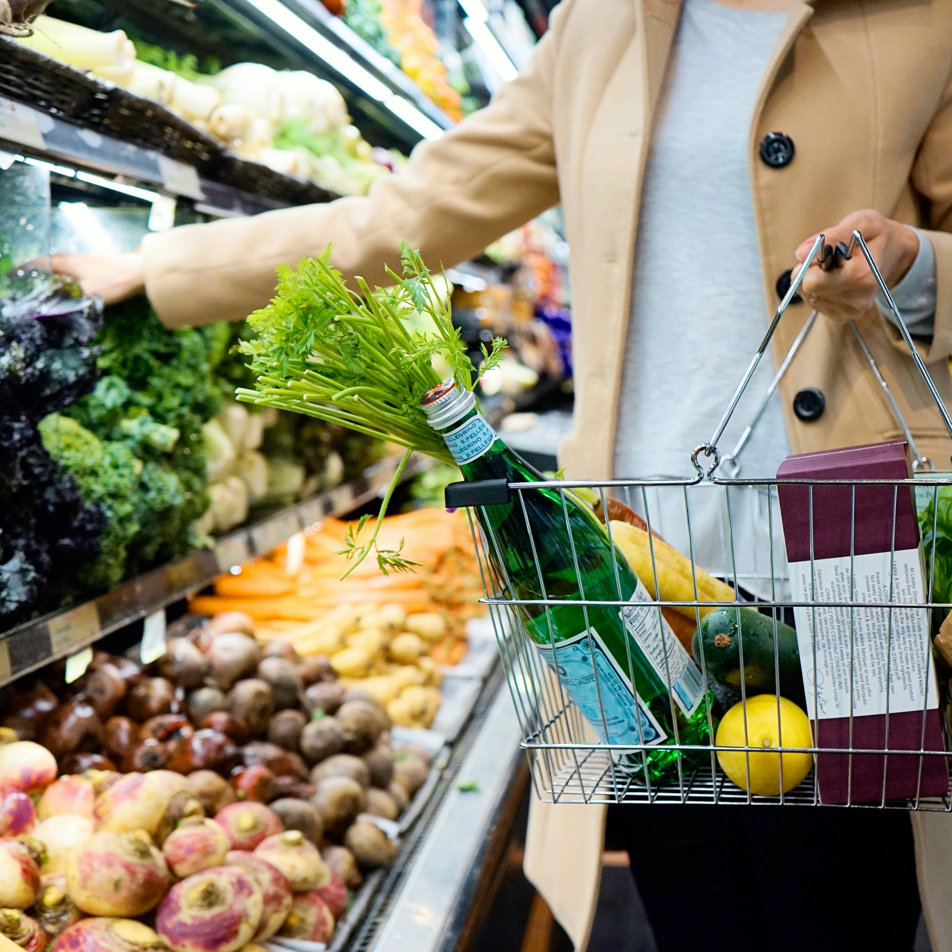 Shopper browsing grocery aisle with wire basket of fresh produce