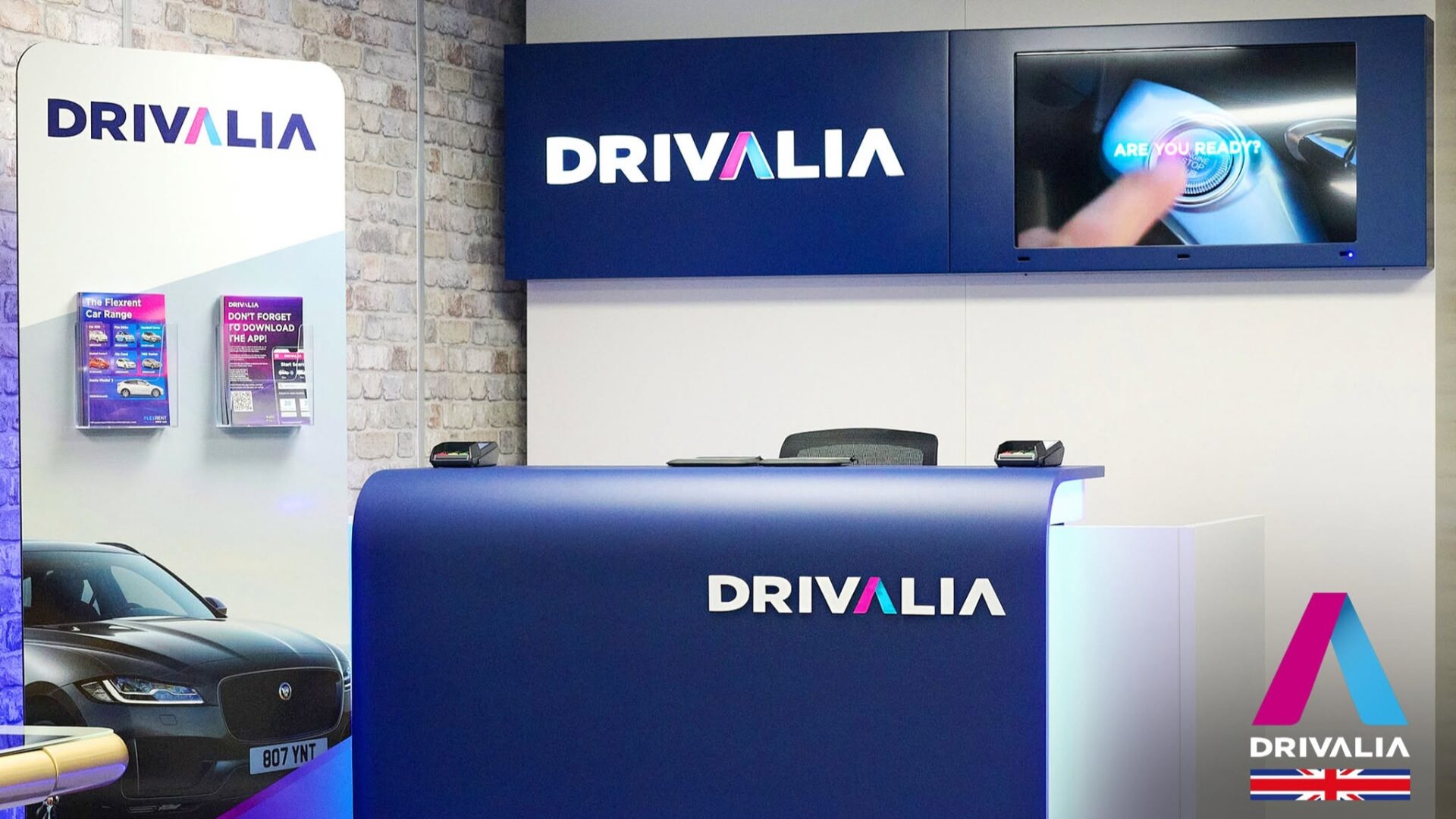 Drivalia car hire rental desk with branded signage and promotional materials at a UK location.